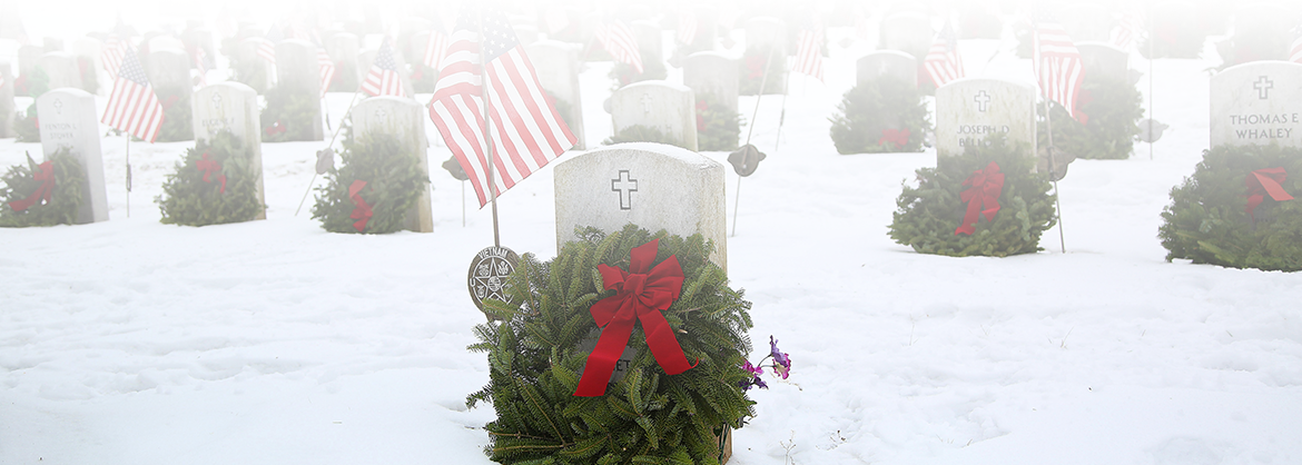 Snow-covered graves decorated with wreaths and American flags for Wreaths Across America